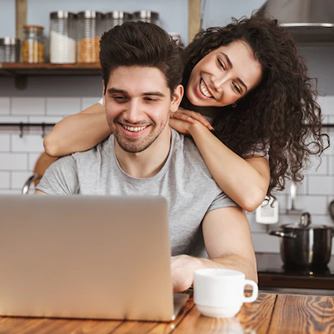 Foto de mulher jovem abraçada ao homem, ammbos sorrindo e olhando para a tela do laptop